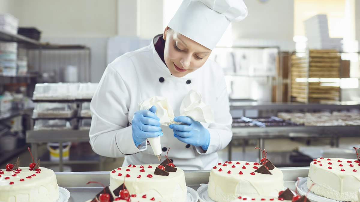 Aluna do curso de confeitaria do SENAC preparando bolo decorado com técnicas profissionais