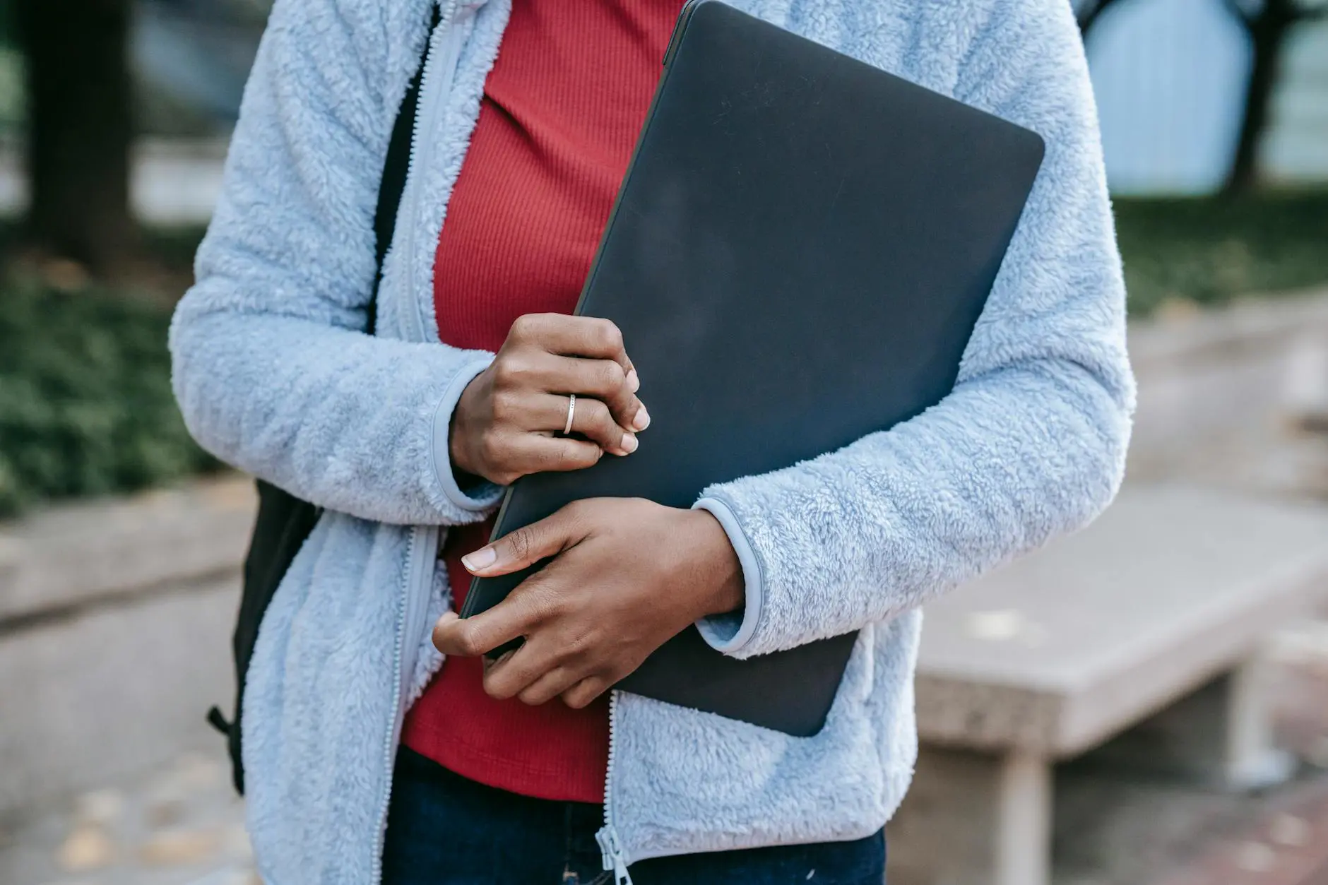 Crop anonymous young African American female student in warm casual clothes and with backpack standing in campus park wi